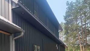 A modern building with a gravel driveway, metal siding, and a small garden area. - New Waterfront Flowage to Full Rec Lake Home On UTV Sled Trails Sleeps 10 (Mountain)