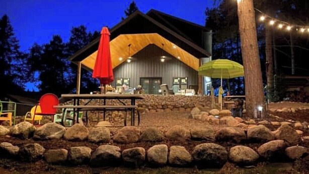A rustic lodge with a wooden exterior, a stone-paved patio, and string lights. - New Waterfront Flowage to Full Rec Lake Home On UTV Sled Trails Sleeps 10 (Mountain)