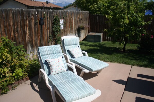 Dos sillones de descanso con cojines a rayas, una valla de madera y un césped.