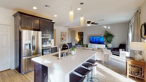 Una cocina moderna con electrodomésticos de acero inoxidable, una isla central con taburetes y un área de comedor con televisor y asientos.