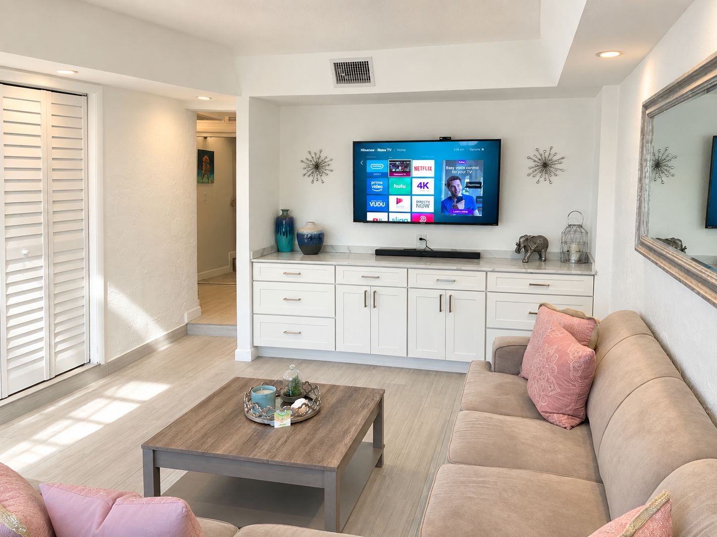 A modern living room with a flat-screen TV mounted on the wall, a sofa, a coffee table, and a cabinet with decorative items.