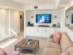 A modern living room with a flat-screen TV mounted on the wall, a sofa, a coffee table, and a cabinet with decorative items. - Beautiful Updated Kawama Townhouse.  Marina, boat ramp, lagoon and pools. (Key Largo)