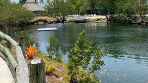 A serene lakeside view with a wooden dock, lush greenery, and a thatched-roof building. - Beautiful Updated Kawama Townhouse.  Marina, boat ramp, lagoon and pools. (Key Largo)