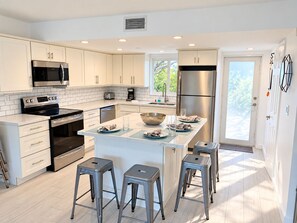 A modern kitchen with white cabinetry, stainless steel appliances, and a central island with stools. - Beautiful Updated Kawama Townhouse.  Marina, boat ramp, lagoon and pools. (Key Largo)