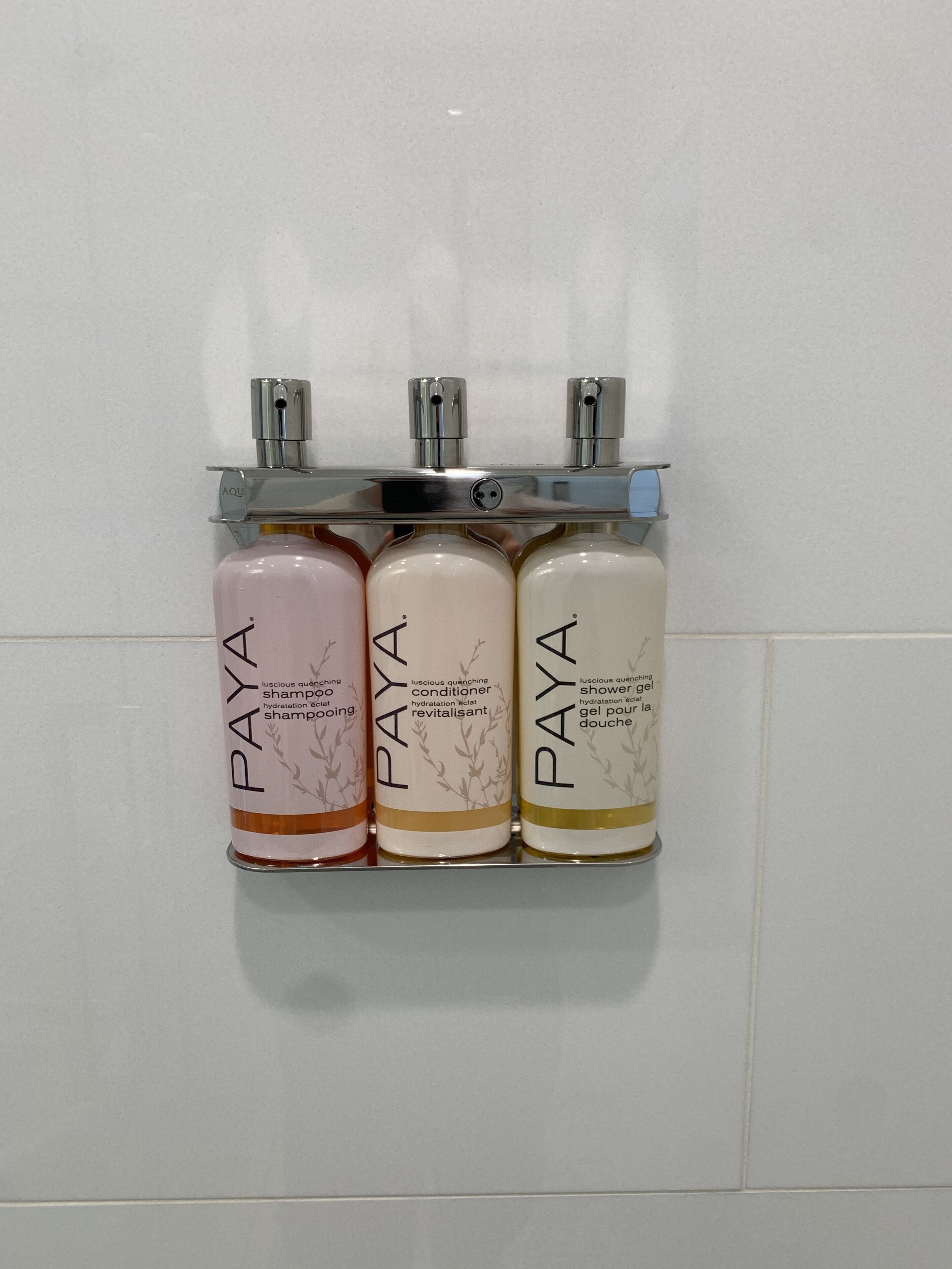 Three bottles of Paya shampoo and conditioner on a wall-mounted rack.
