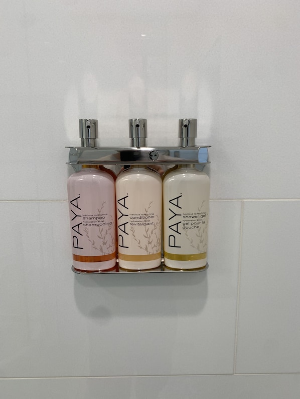 Three bottles of Paya shampoo and conditioner on a wall-mounted rack.