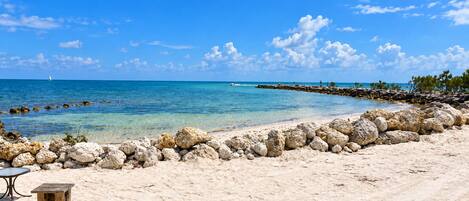 A beach with clear blue water, a rocky breakwater, and a wooden table.