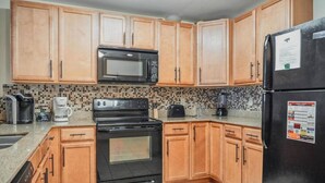 Una cocina con armarios de madera, un microondas negro, una estufa y un refrigerador.