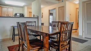 Comedor con mesa y sillas de madera, cocina al fondo y una puerta que da a otra habitación.