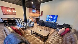 A spacious living area with a brown leather sofa, a wooden coffee table, and a television mounted on the wall. - Historic FireHouse Lodge Very Cool! (COTTER)