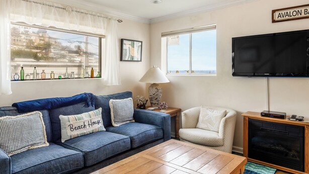 A living room with a blue sofa, a wooden coffee table, a TV, and a fireplace. - 220W: Lovely Avalon home + walking distance to the beach, restaurants and more. (Avalon)