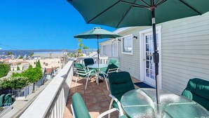 A balcony with green chairs and a table, overlooking a scenic view. - 220W: Lovely Avalon home + walking distance to the beach, restaurants and more. (Avalon)