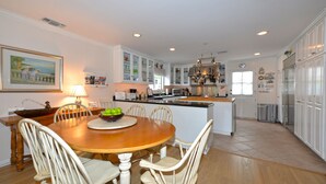 A spacious kitchen with a dining area, featuring a wooden table and chairs, a kitchen island, and white cabinetry. - 220W: Lovely Avalon home + walking distance to the beach, restaurants and more. (Avalon)