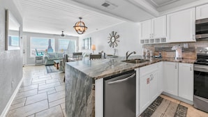 Una cocina moderna con armarios blancos, una isla de mármol, electrodomésticos de acero inoxidable y un comedor con vistas.
