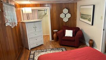 A room with wooden paneling, a white dresser, a red sofa, a bed with a red blanket, a hexagonal wall decoration, and a framed picture on the wall.