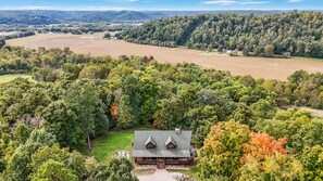 A lodge with a central building surrounded by dense forest, a large open field, and a hilly landscape in the background.