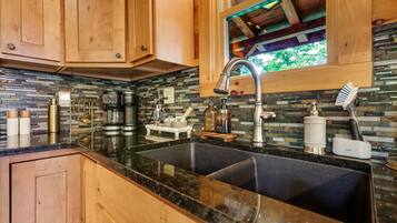 Une cuisine avec des meubles en bois, un plan de travail en granit noir, un évier en acier inoxydable et une fenêtre donnant sur un paysage verdoyant.