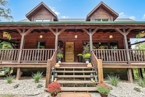 A wooden cabin with a porch, a front door, and a staircase leading up to it. - Arrow Ridge at Hocking Hills (Sugar Grove)