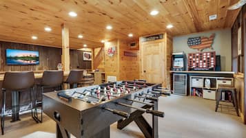 A cozy indoor space with a foosball table, bar area, and a television screen.