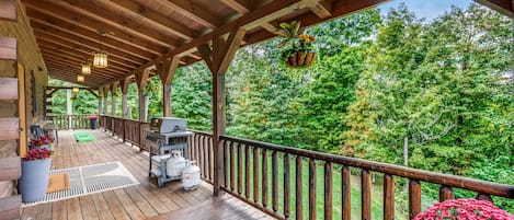 Eine überdachte Holzterrasse mit Grill, Sitzgelegenheiten und Blick auf einen Wald.