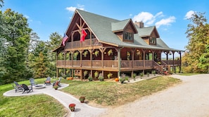 A large wooden cabin with a balcony, a covered porch, and a driveway leading to the entrance. - Arrow Ridge at Hocking Hills (Sugar Grove)