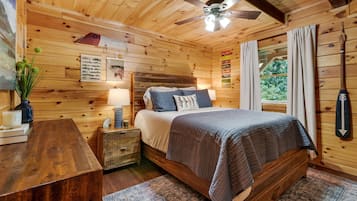 A wooden cabin bedroom with a bed, nightstand, lamp, and a ceiling fan.