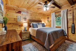 Un dormitorio de cabaña de madera con cama, mesita de noche, lámpara y ventilador de techo.