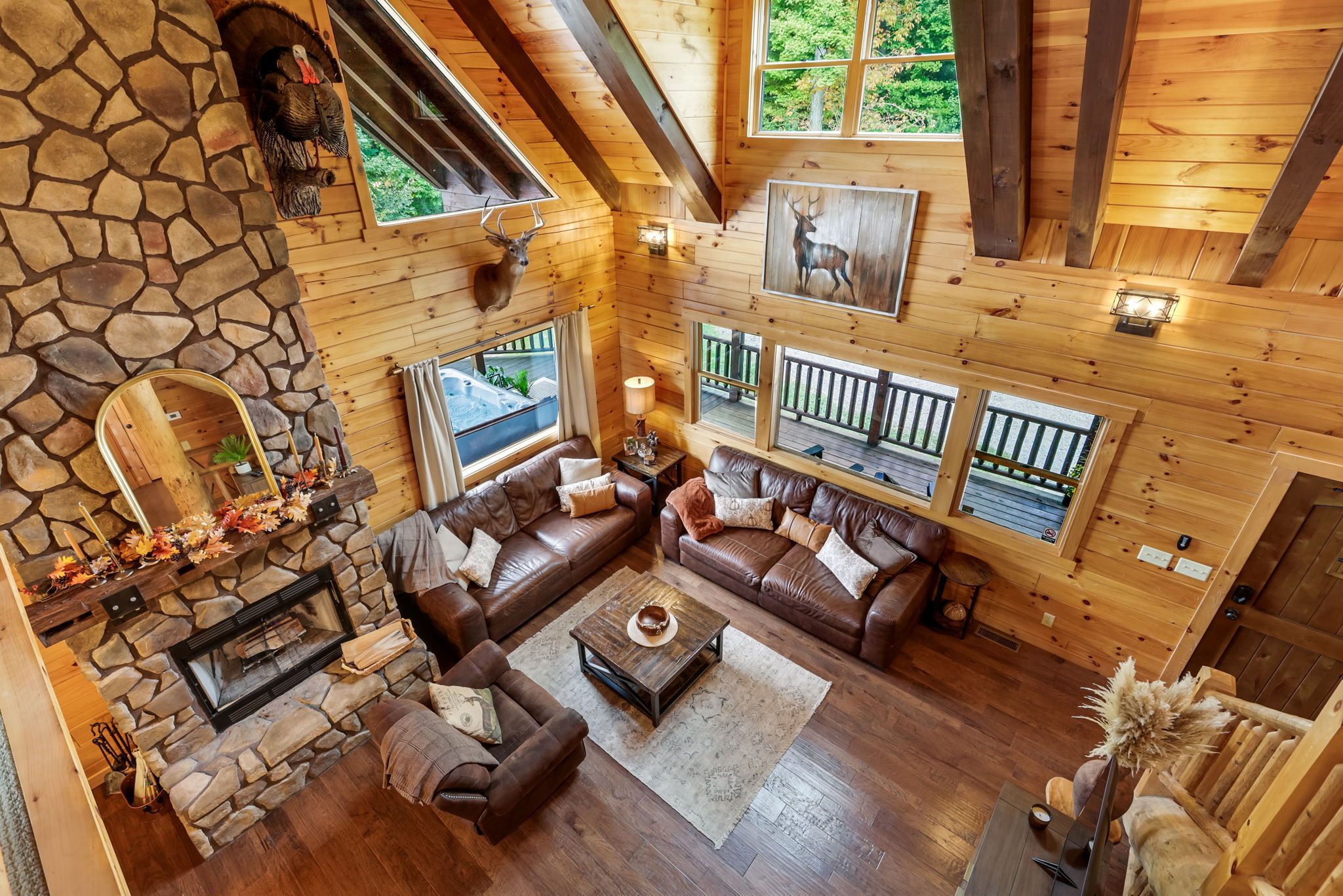 A spacious living area with a stone fireplace, leather sofas, and a view of a hot tub through large windows.