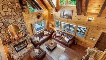 A spacious living area with a stone fireplace, leather sofas, and a view of a hot tub through large windows.
