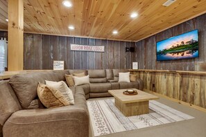 Una sala de estar acogedora con un sofá modular, una mesa de centro y un televisor montado que muestra un paisaje pintoresco.