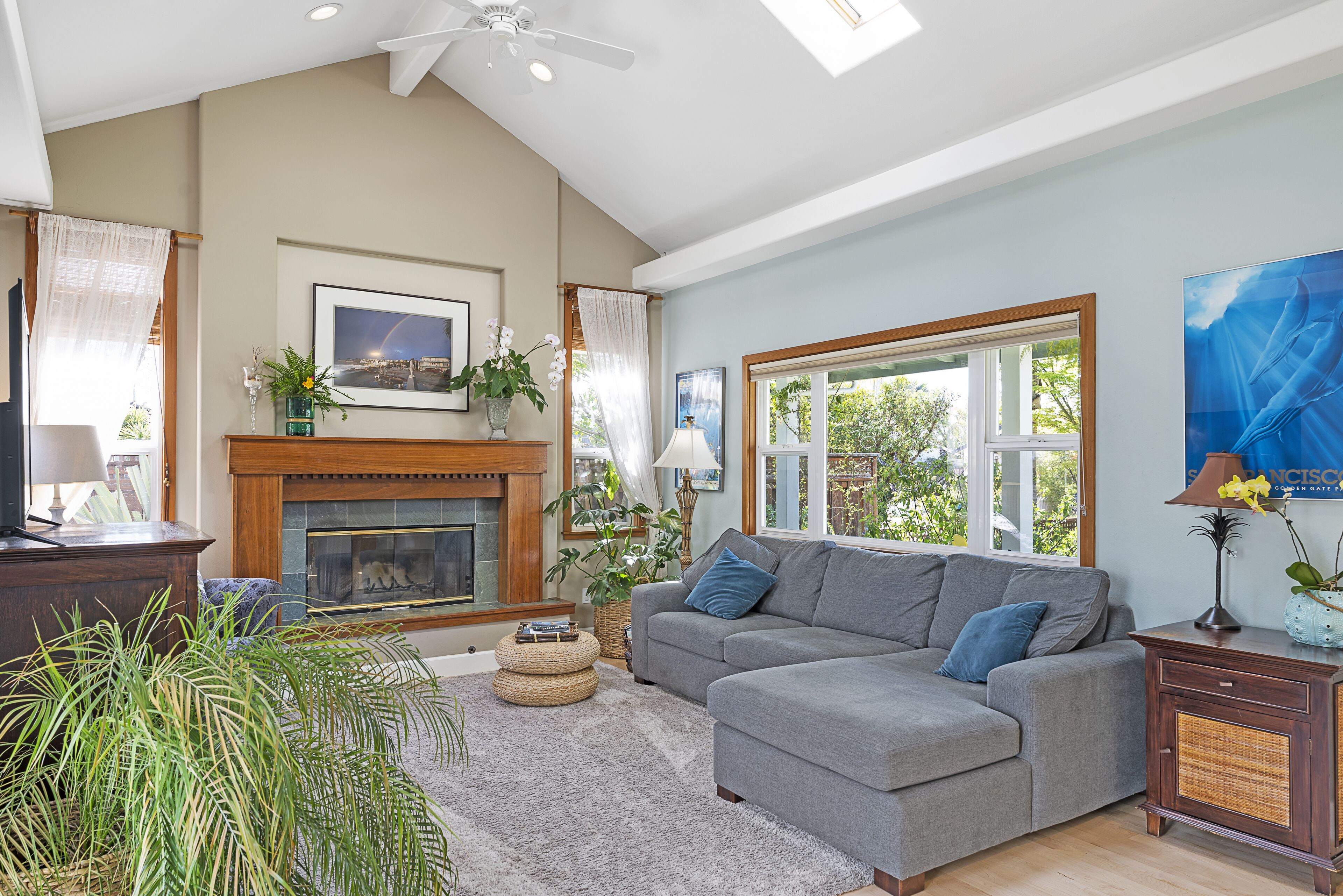 A living room with a fireplace, a grey sofa, and a large window.