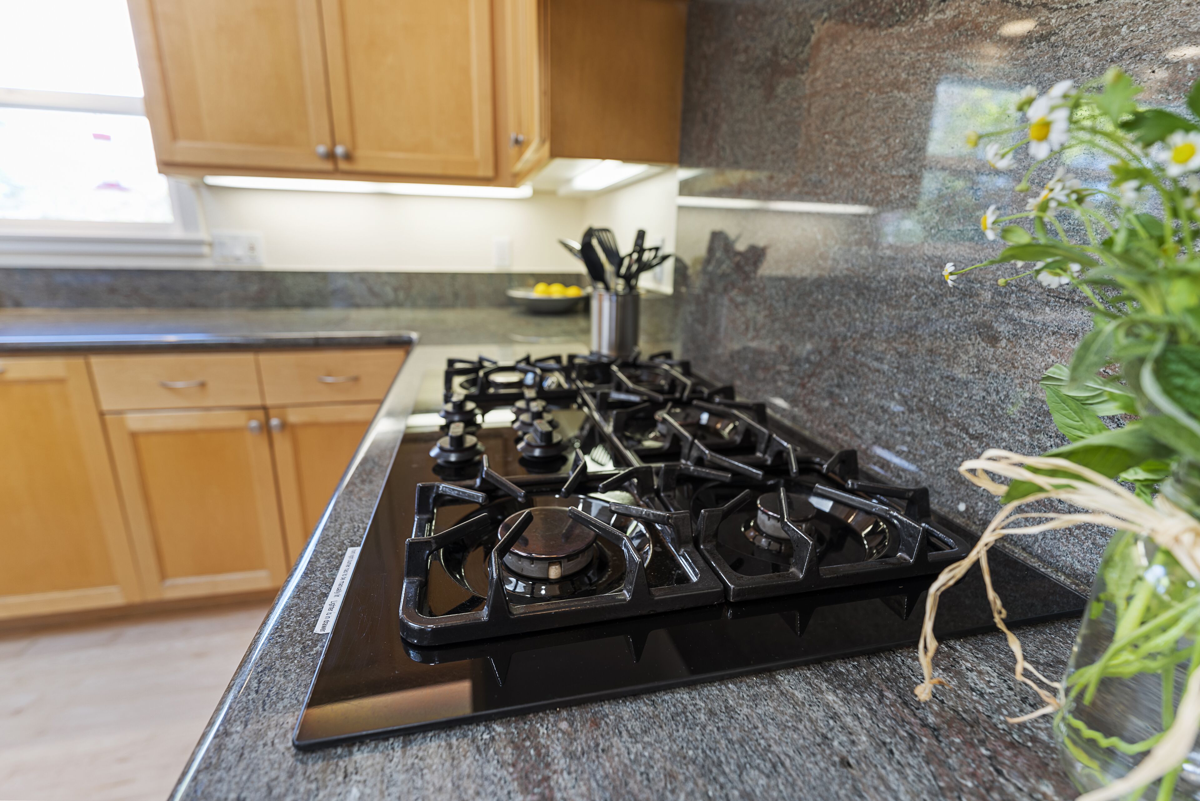 A kitchen with a black stove, wooden cabinets, and a granite countertop.