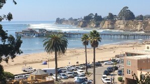 A beach with a parking lot, a pier, and buildings in the background.