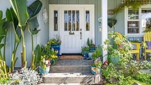 A front porch with a white door, potted plants, and a yellow chair.