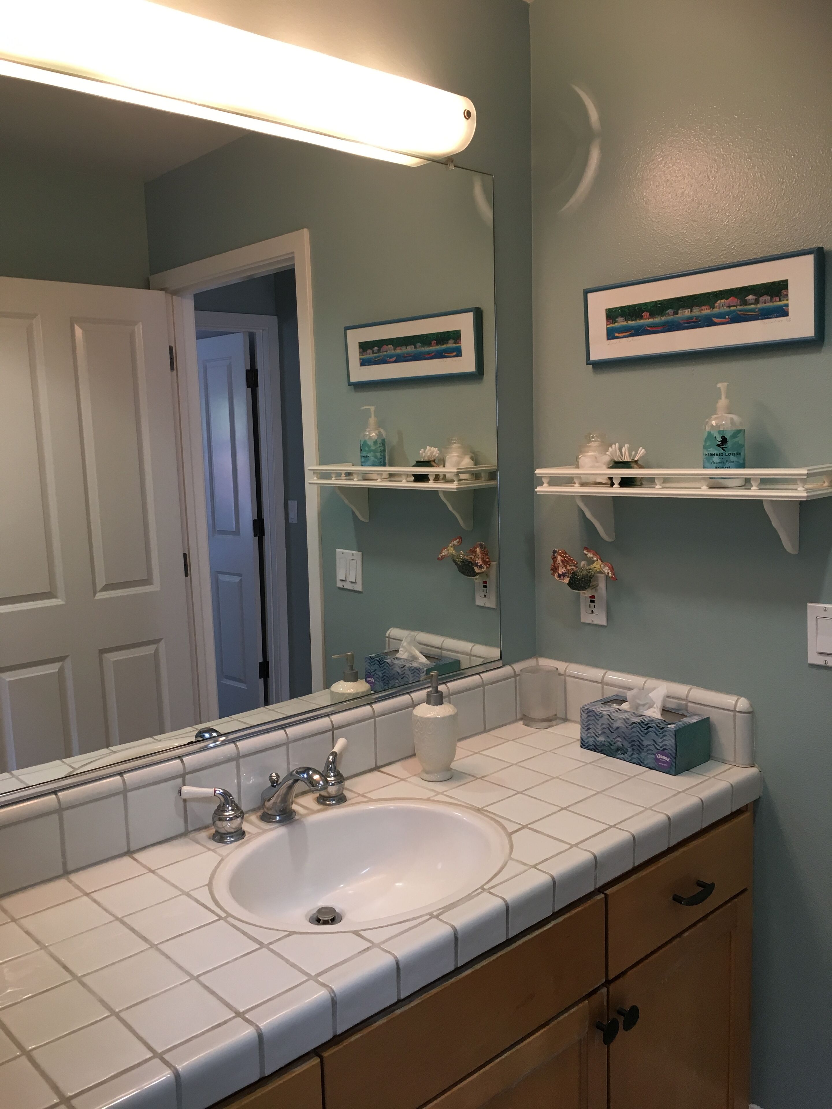 A bathroom with a white sink, a mirror, two shelves with toiletries, and a door leading to another room.