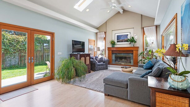 A spacious living room with a fireplace, a television, and a large window overlooking a garden.