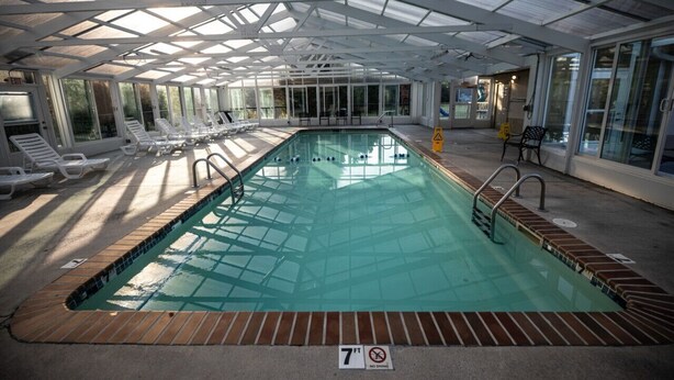 Una piscina interna con pareti in vetro trasparente, illuminata dalla luce naturale e pavimento piastrellato.