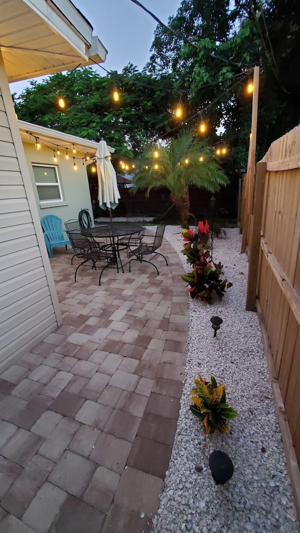 Relax in a serene outdoor space with a dining table, comfortable seating, and lush greenery.