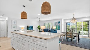 A modern kitchen with a large island, pendant lights, and a dining area with a view.
