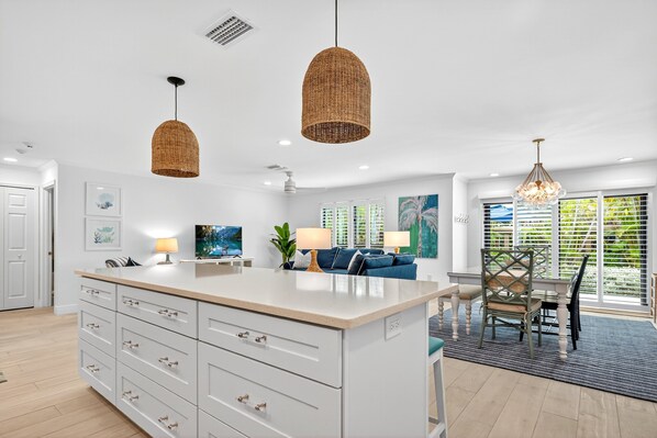 A modern kitchen with a large island, pendant lights, and a dining area with a view.