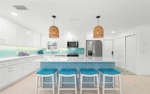 A modern kitchen with white cabinets, a central island with bar stools, and a stainless steel refrigerator.