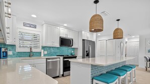 A modern kitchen with white cabinets, a central island with teal bar stools, a microwave, a refrigerator, and a dishwasher.