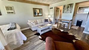 Una sala de estar con un sofá, una mesa de centro, un tapete de cuero de vaca y un comedor con mesa y sillas.