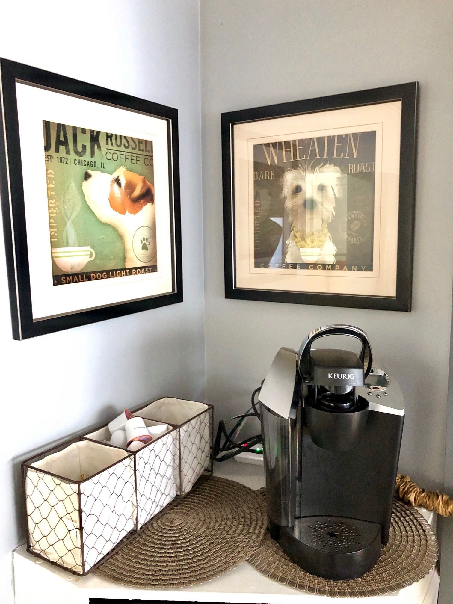 A coffee maker on a counter with a framed Jack Russell Terrier coffee advertisement and a framed Wheatenn dog roast advertisement.