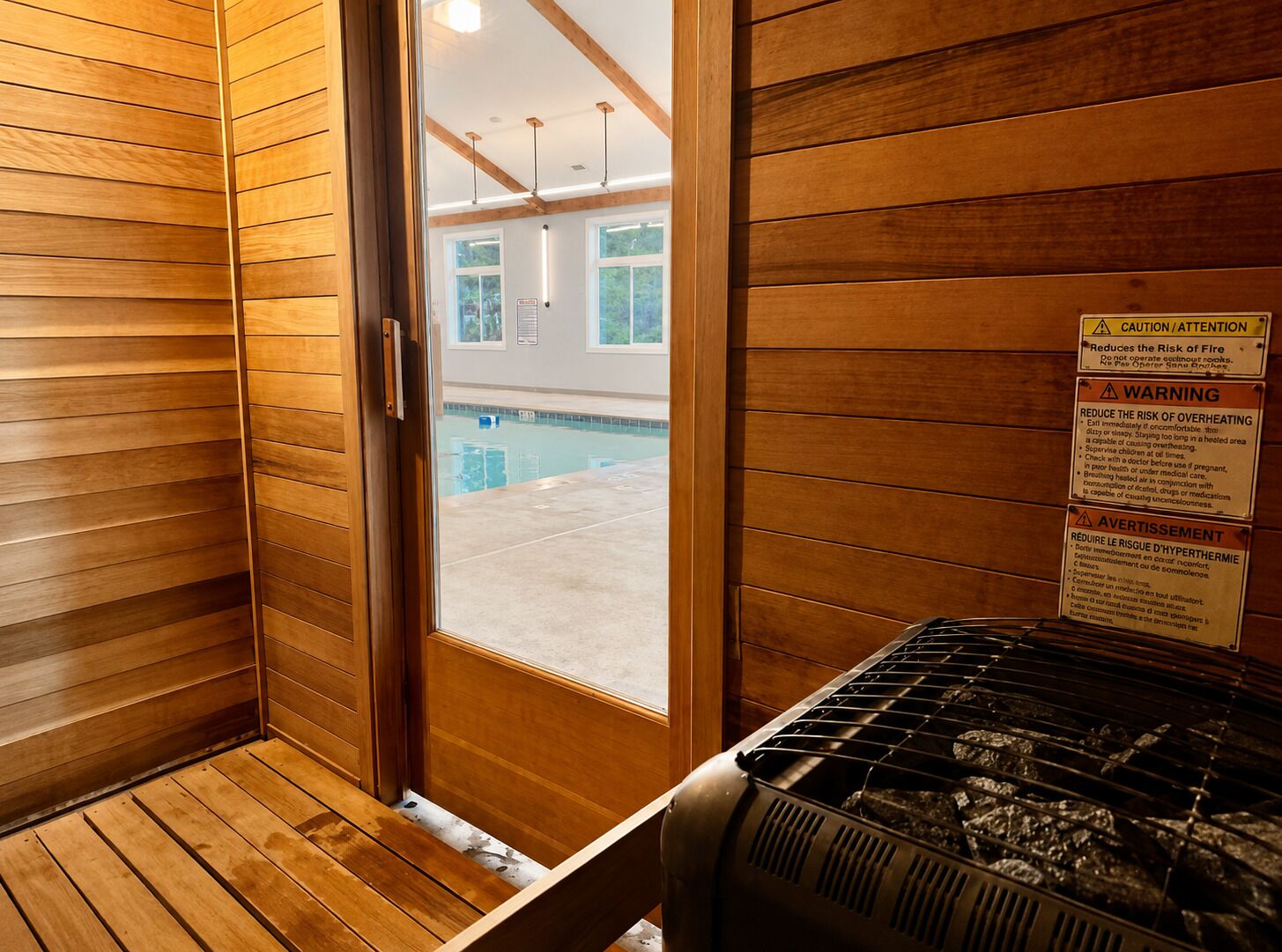 Un sauna aux murs en bois, doté d’une porte en verre et d’un panneau d’avertissement.