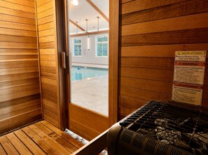 Una sala de sauna con paredes de madera, una puerta de vidrio y un cartel de advertencia.