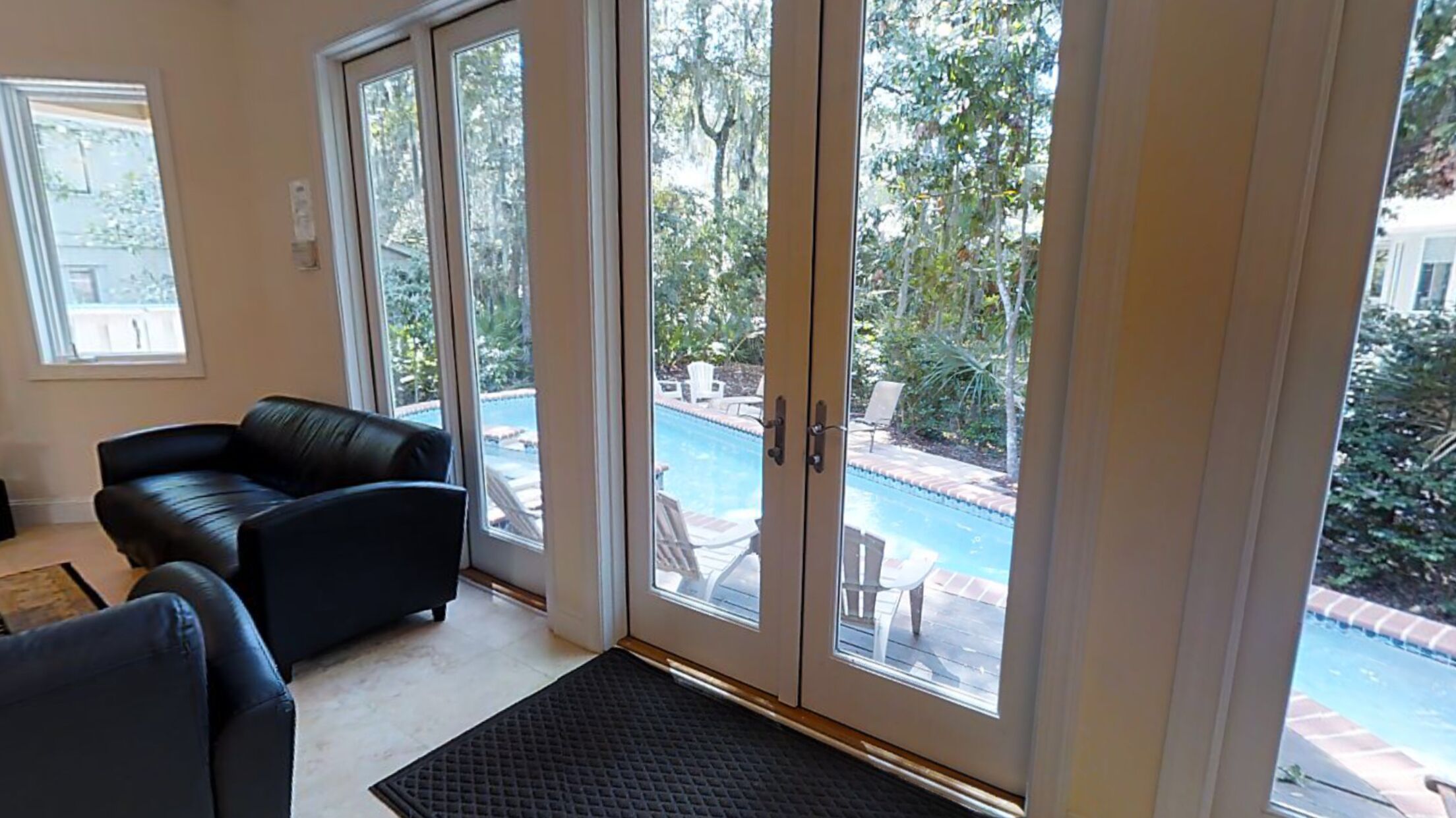 A room with a black leather sofa, a glass door leading to a pool area, and a view of the outdoors.