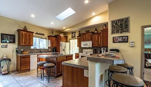 A kitchen with wooden cabinets, a central island with stools, a microwave, and a refrigerator.