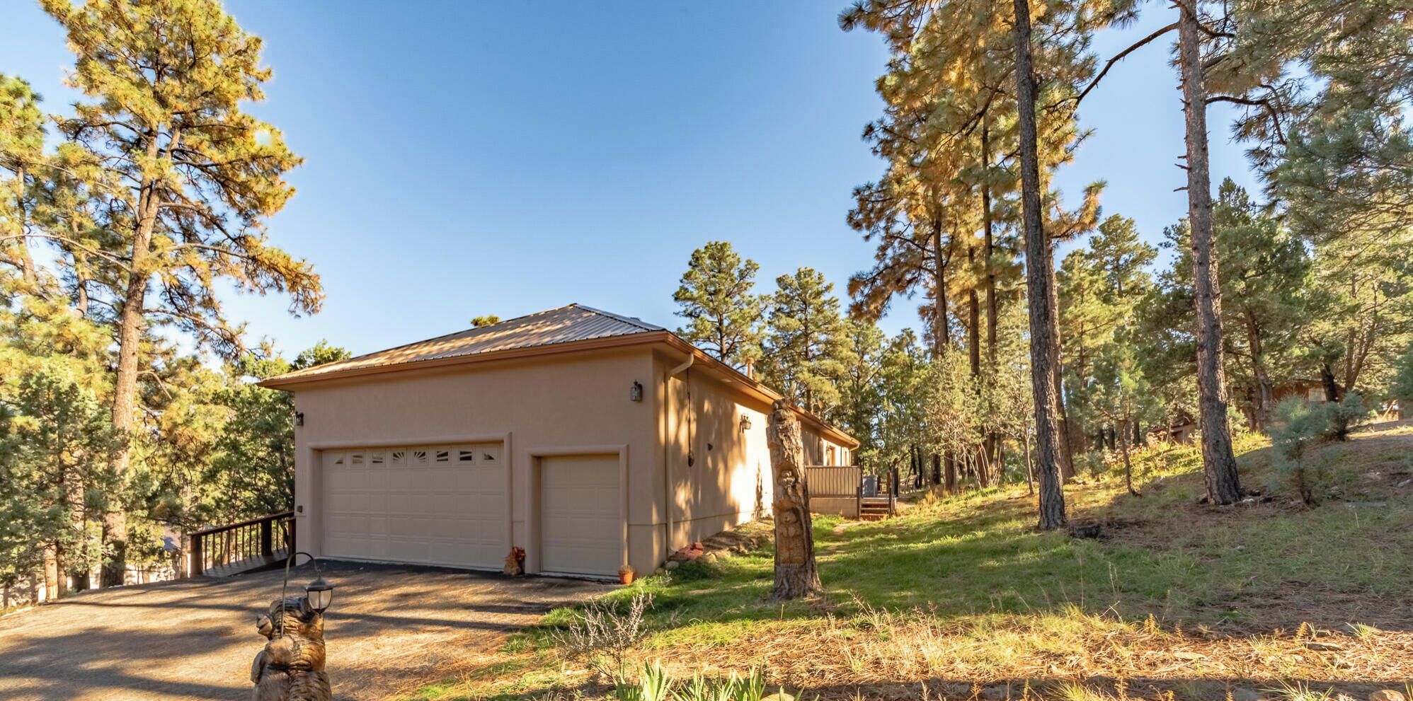 A single-story house with a garage, surrounded by tall pine trees.