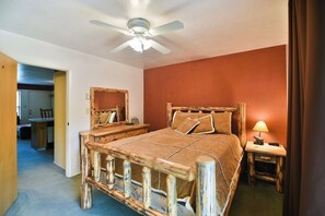 A bedroom with a wooden bed frame, a ceiling fan, a bedside table with a lamp, and a mirror on the wall. - Classic 1BR Wolf Lodge close to hot tub (Eden)